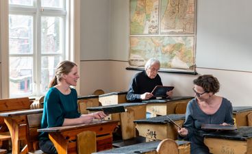 en gruppe mennesker som sitter ved pulter i et rom en gruppe mennesker som sitter ved pulter i et rom